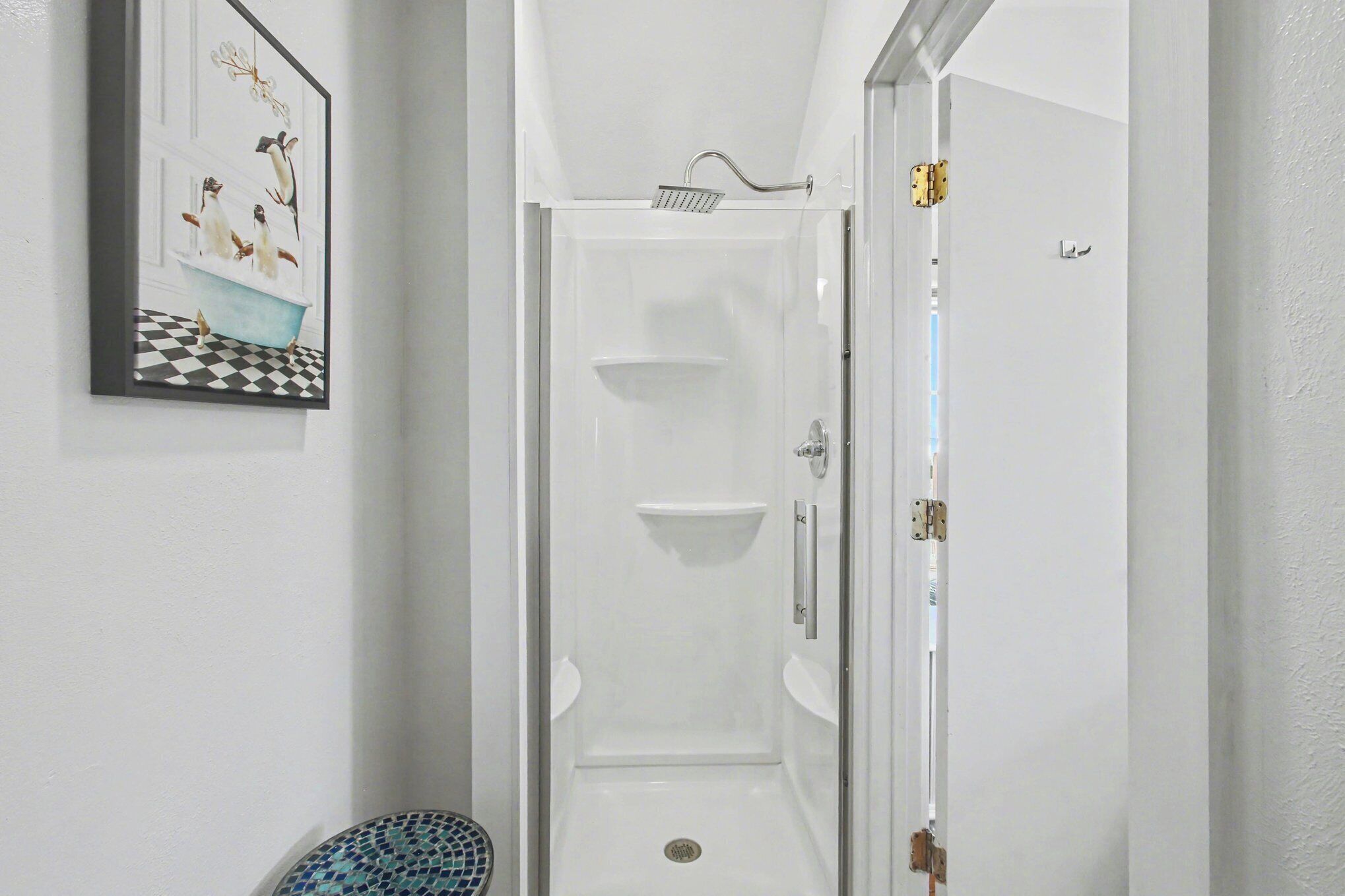 A narrow hallway leading to a shower area with a tiled floor, a wall-mounted shelf, and a door with a handle.