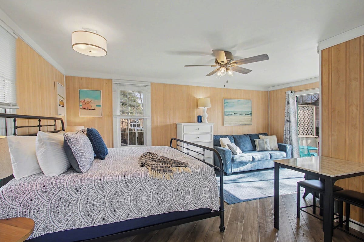 A bedroom with a bed, a desk, a chair, a ceiling fan, and a window with blinds.