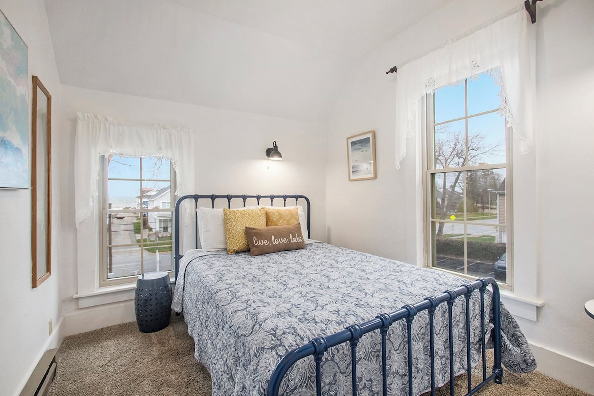 A bedroom with a bed, two windows, a lamp, and a framed picture on the wall.