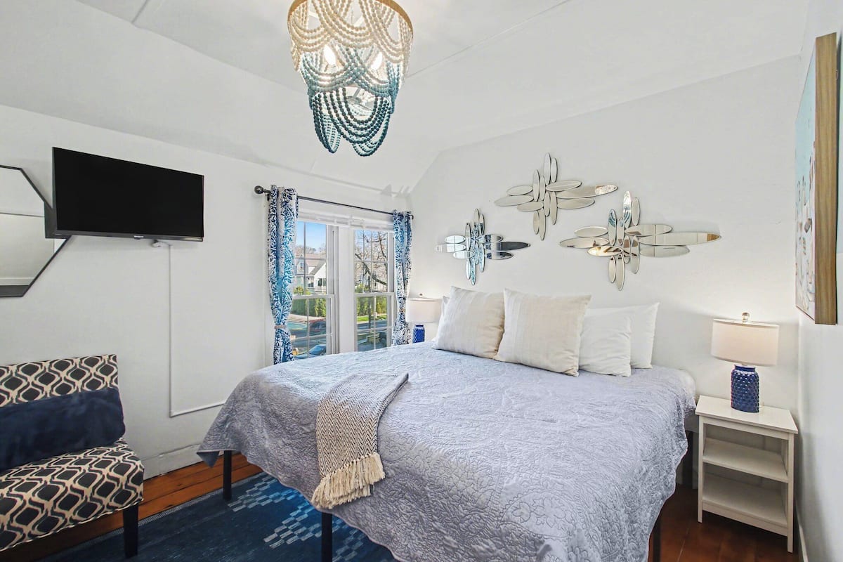 A bedroom with a bed, a TV, a decorative ceiling light, a wall-mounted clock, and a window with curtains.