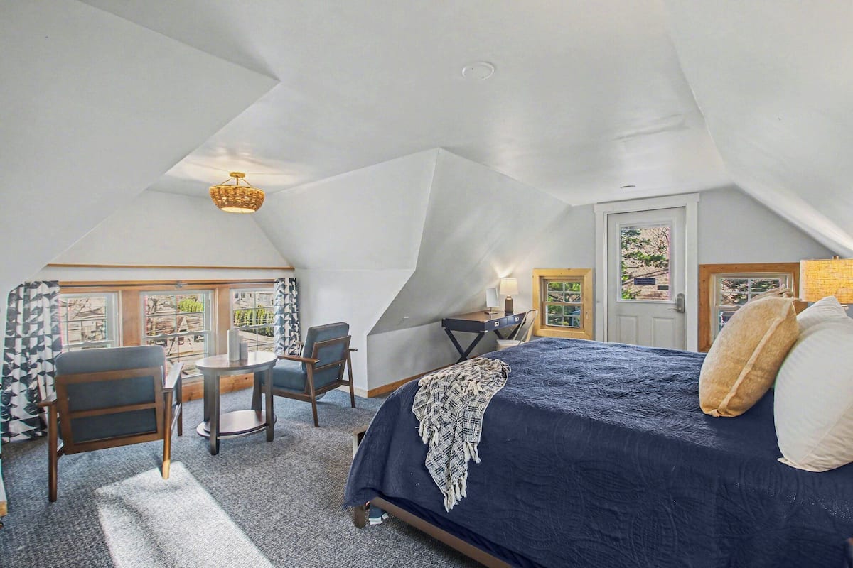 A bedroom with a bed, a desk, a chair, and a view through a window.