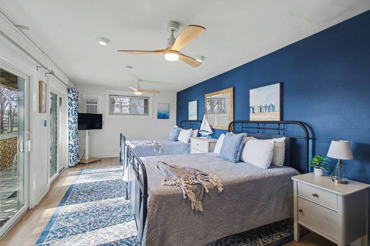 A bedroom with two beds, a ceiling fan, a TV, and a large window.