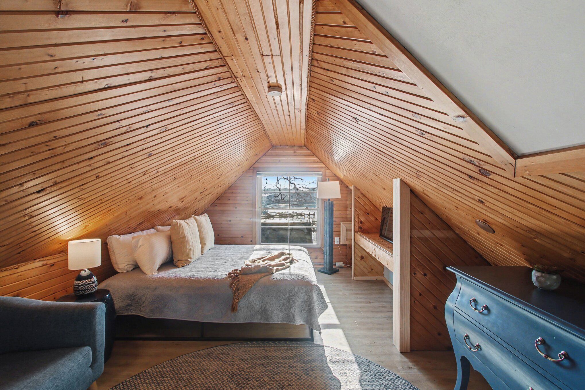Une chambre avec un plafond en pente, un lit, une commode et une fenêtre donnant sur un beau paysage.
