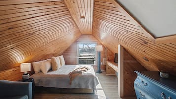 Une chambre avec un plafond en pente, un lit, une commode et une fenêtre donnant sur un beau paysage.