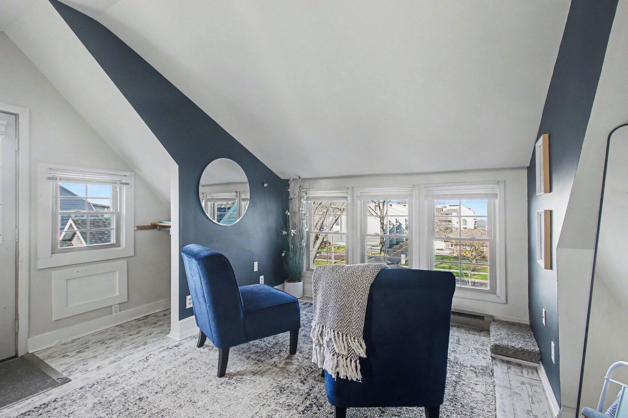 A room with a sloped ceiling, a large window, a blue chair, and a potted plant.