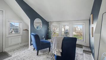 Una habitación con techo inclinado, un ventanal grande, una silla azul y una planta en maceta.