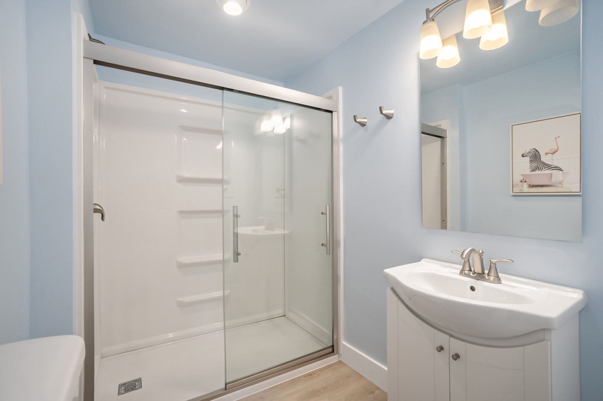 Un baño moderno con cabina de ducha de vidrio, un lavabo blanco y un cuadro en la pared.