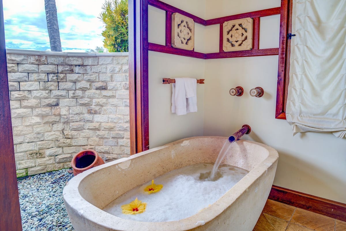 A stone bathtub with water flowing, two towels on a rack, and decorative wall panels.
