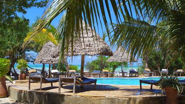 A poolside area with lounge chairs and thatched umbrellas, overlooking a clear blue sea. - Mbuyuni Beach Village - Bungalows (Jambiani)