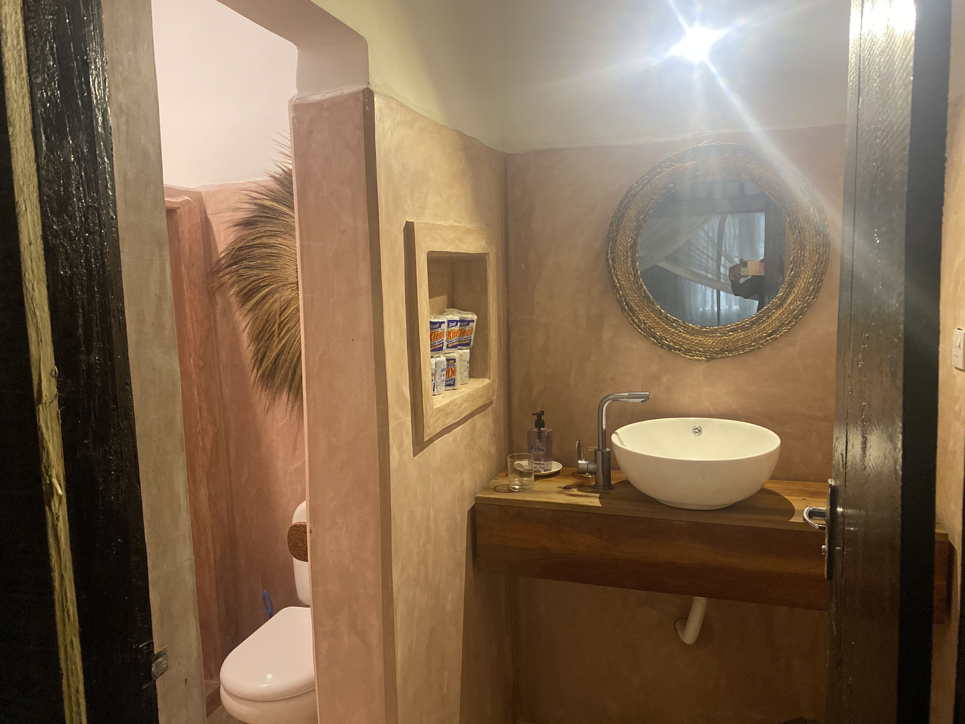 A bathroom with a white sink, a mirror, and a shelf with toiletries.