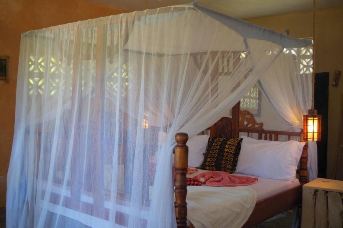 Una cama con cabecera de madera, dosel y lámpara de noche.