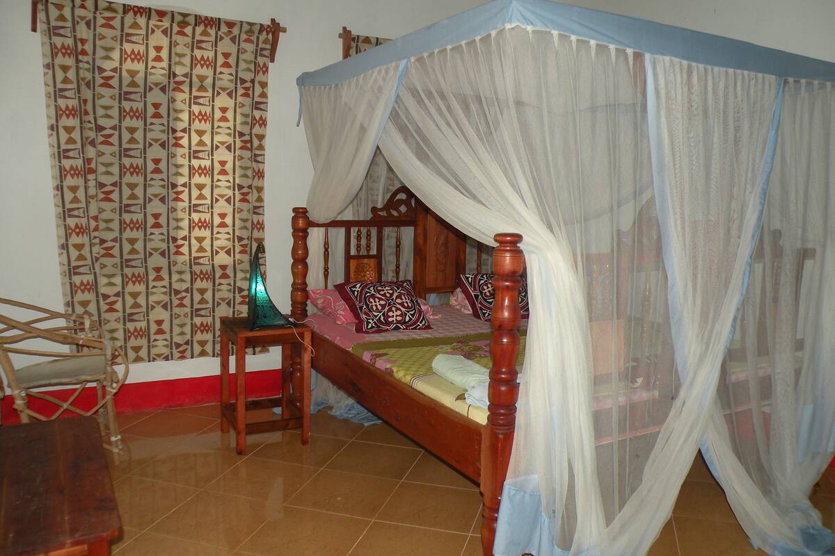 Un dormitorio con una cama de madera, una mesita de noche, una silla y una cortina con estampado geométrico.