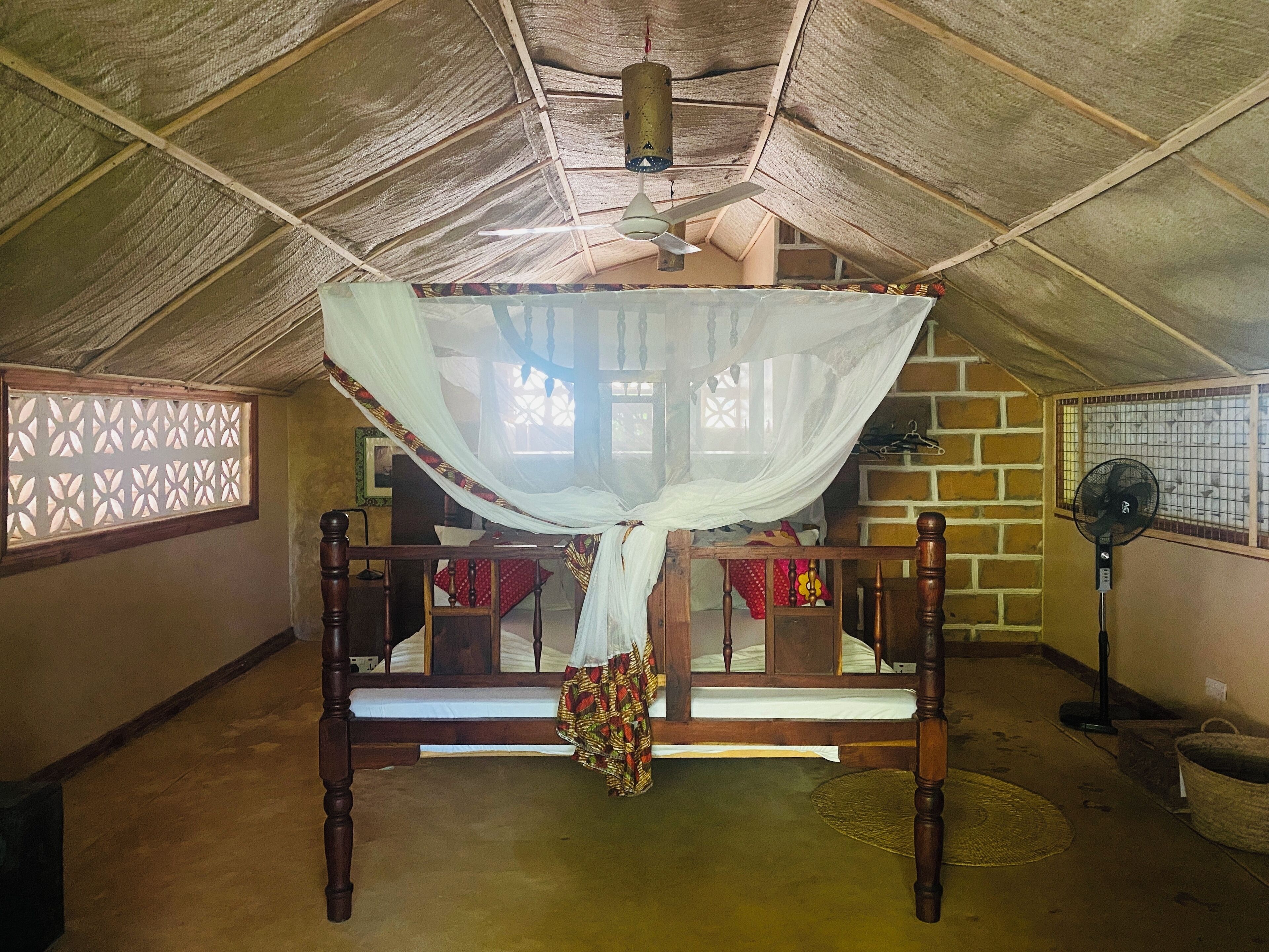 Una habitación tradicional con una cama de madera, mosquitero y ventilador de techo.