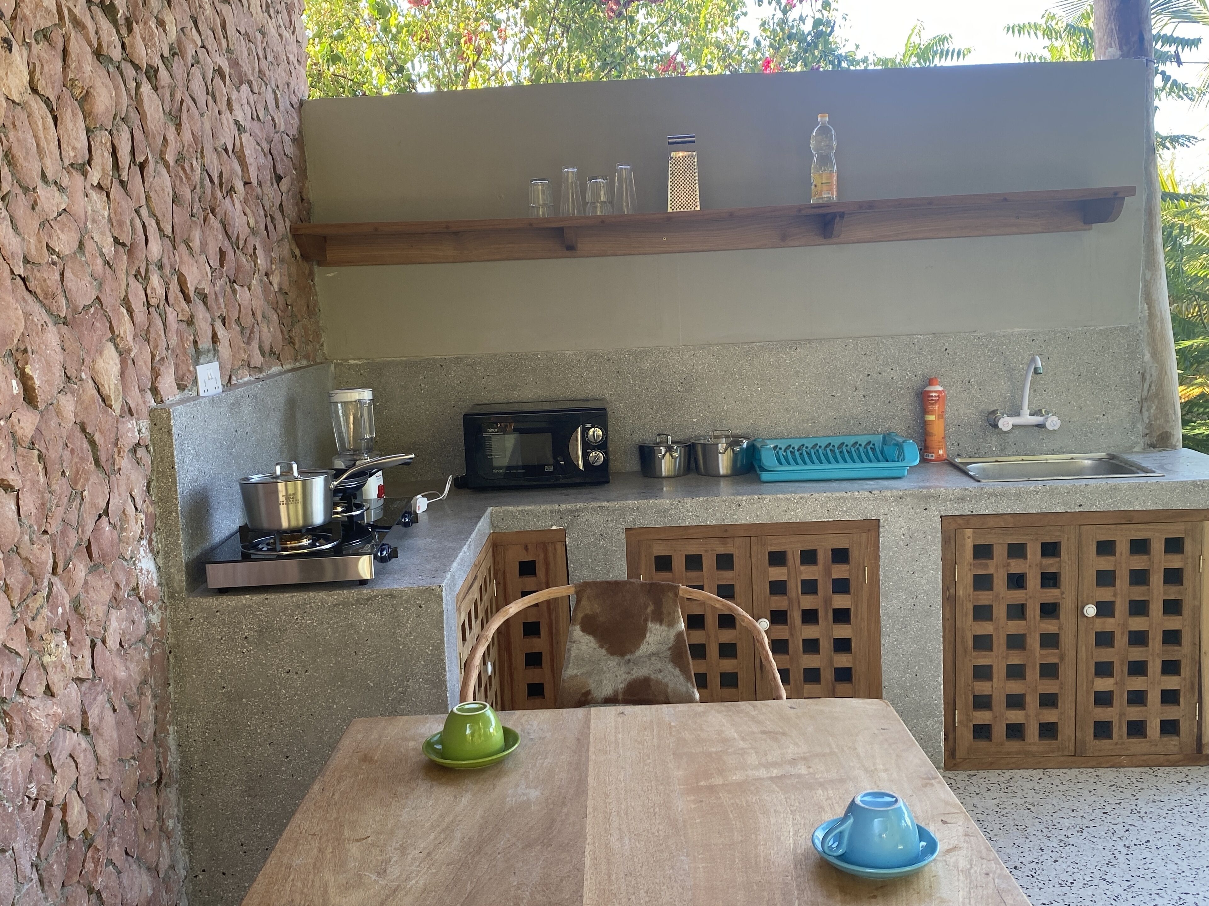 Cocina compacta con estufa a gas, microondas y lavamanos. Hay armarios debajo de la encimera y una pequeña mesa con una silla.