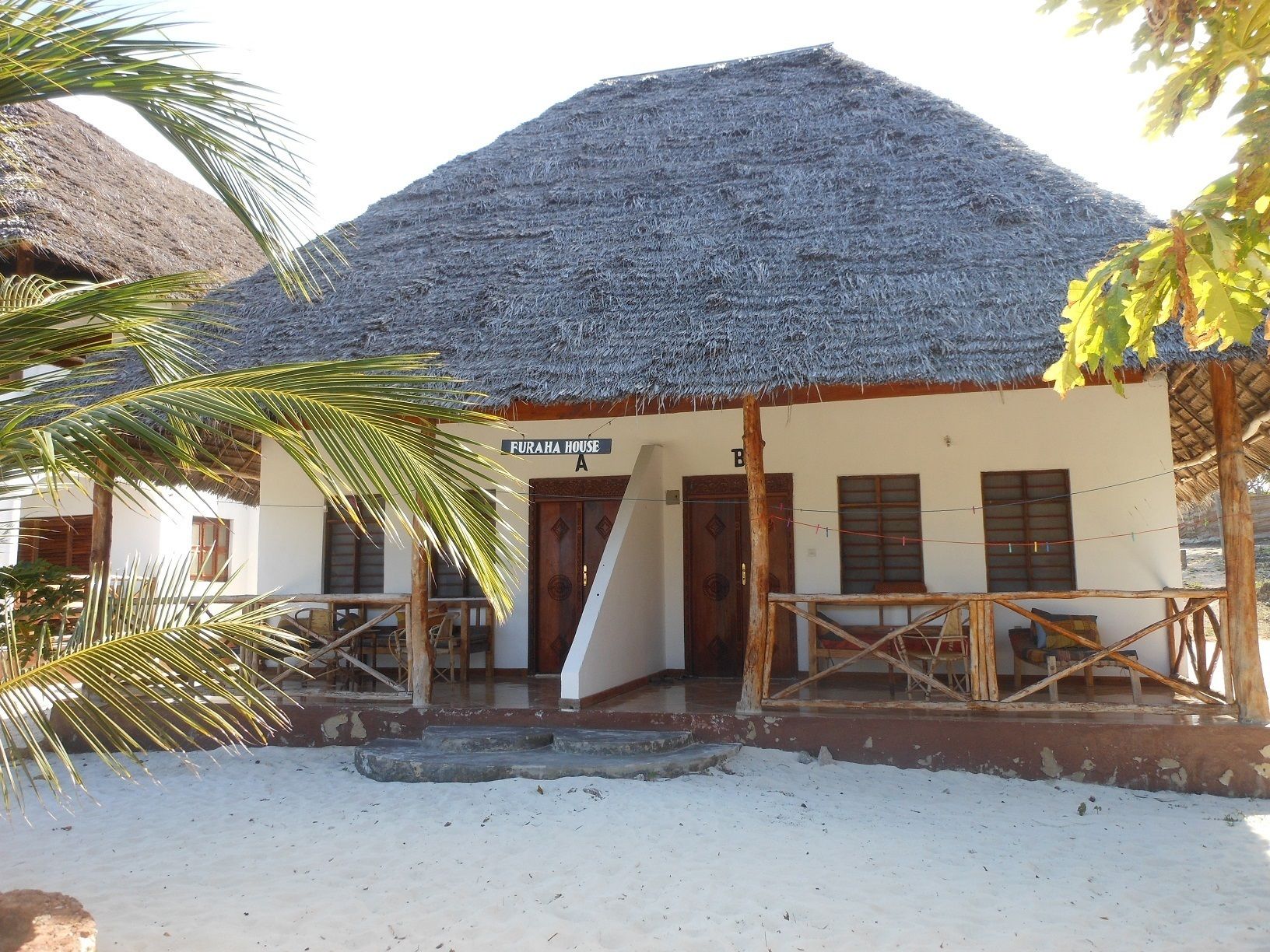 A building with a thatched roof, a sign reading "FURAH HOUSE A", and a wooden staircase leading to the entrance.