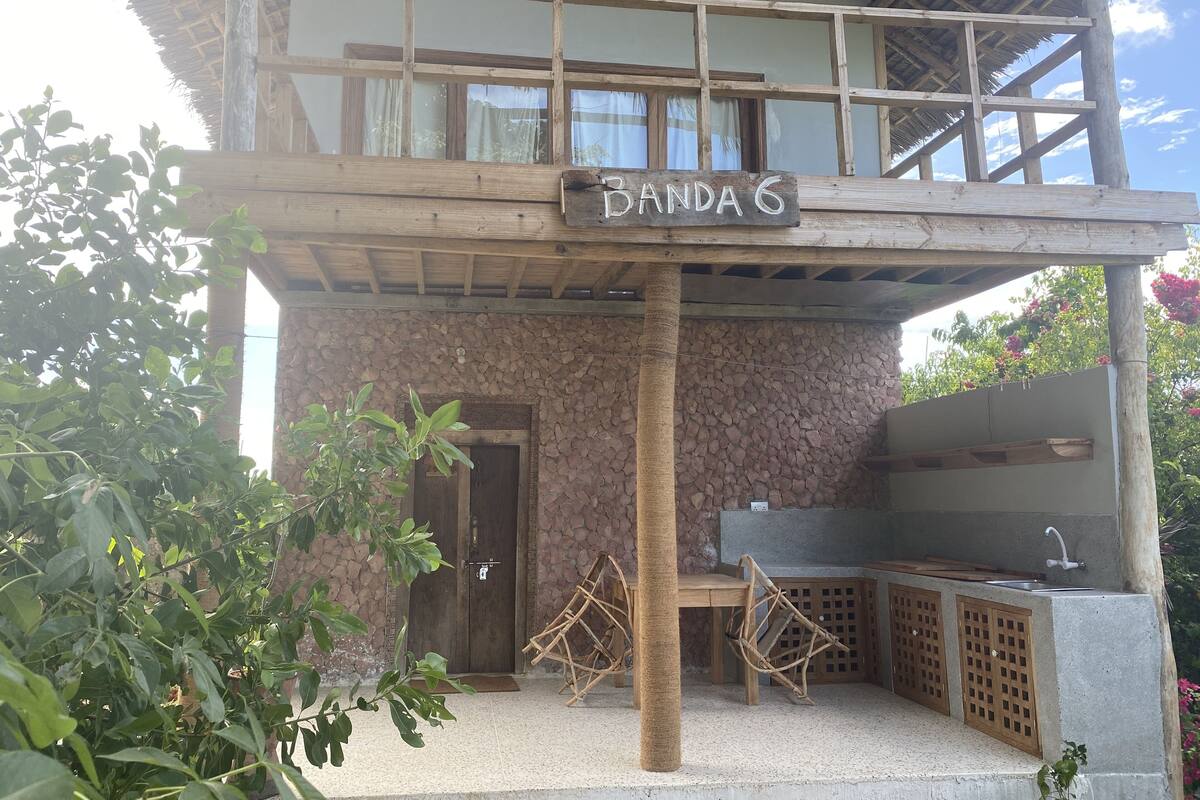 Un edificio rústico con pared de piedra, una terraza de madera y un letrero que dice "BANDA 6".