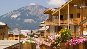 A wooden chalet with a balcony, surrounded by flower boxes and a mountain backdrop. - Madame Vacances - Residence Les Balcons des Airelles (Les Orres)