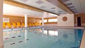 An indoor swimming pool with tiled floors and walls, wooden paneling, and yellow lounge chairs along the poolside. - Madame Vacances - Residence Les Balcons des Airelles (Les Orres)