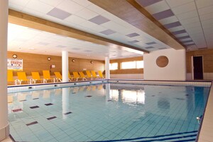 Une piscine intérieure avec des sols et des murs carrelés, un lambris en bois et des chaises longues jaunes disposées le long du bord de la piscine.