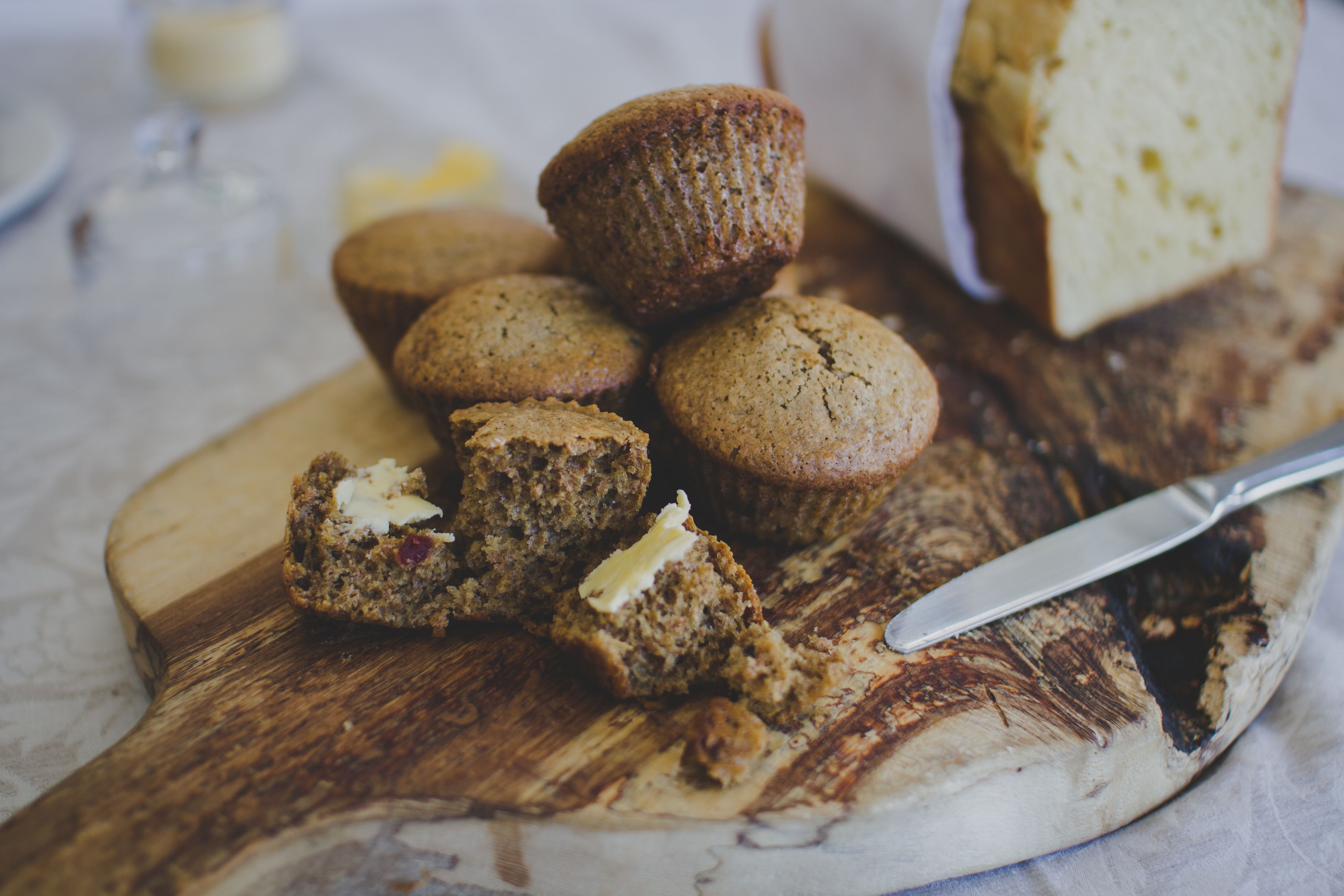 A wooden cutting board with several muffins and a knife.