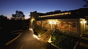 A building with a staircase leading to a covered area with multiple windows, surrounded by a landscaped garden. - Schoone Oordt Country House (Swellendam)