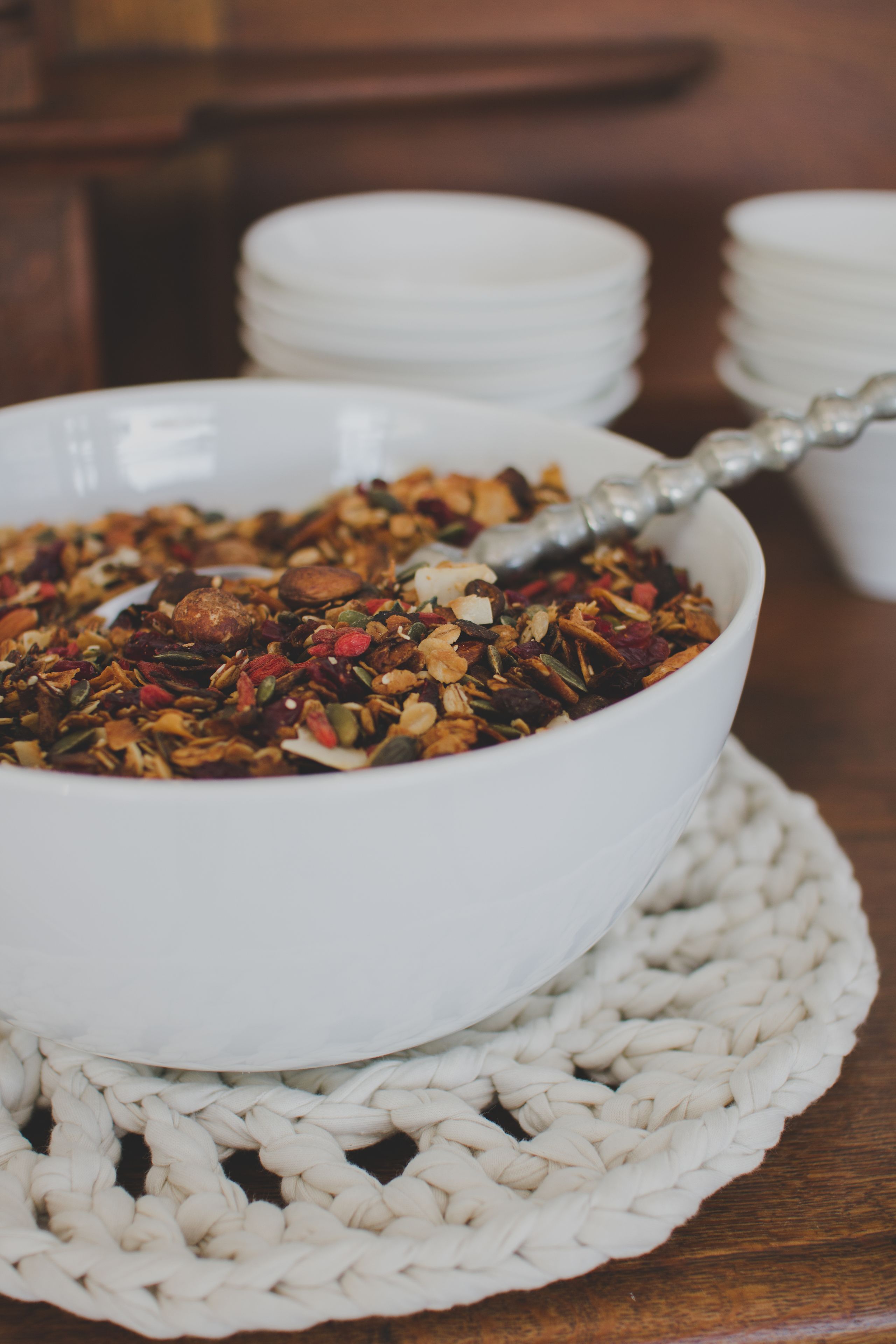 A bowl of granola with a spoon, placed on a woven placemat.