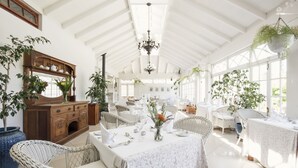 A spacious, well-lit room with high ceilings, white walls, and large windows. There are several dining tables set with white tablecloths and chairs. - Schoone Oordt Country House (Swellendam)