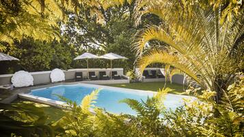 A swimming pool surrounded by lush greenery and white umbrellas.