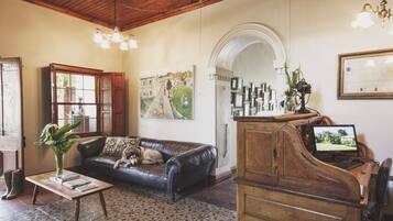 A living room with a black leather sofa, a wooden coffee table, a painting on the wall, a piano, and a chandelier.