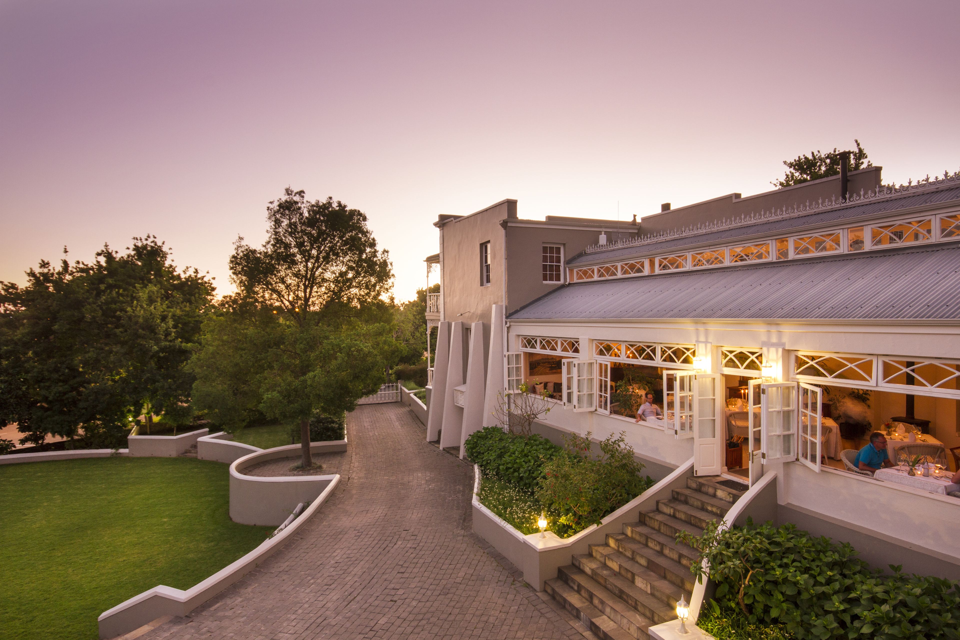 A building with a covered outdoor seating area, a paved walkway, and landscaped gardens.