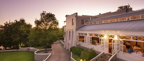 A building with a covered outdoor seating area, a paved walkway, and landscaped gardens.