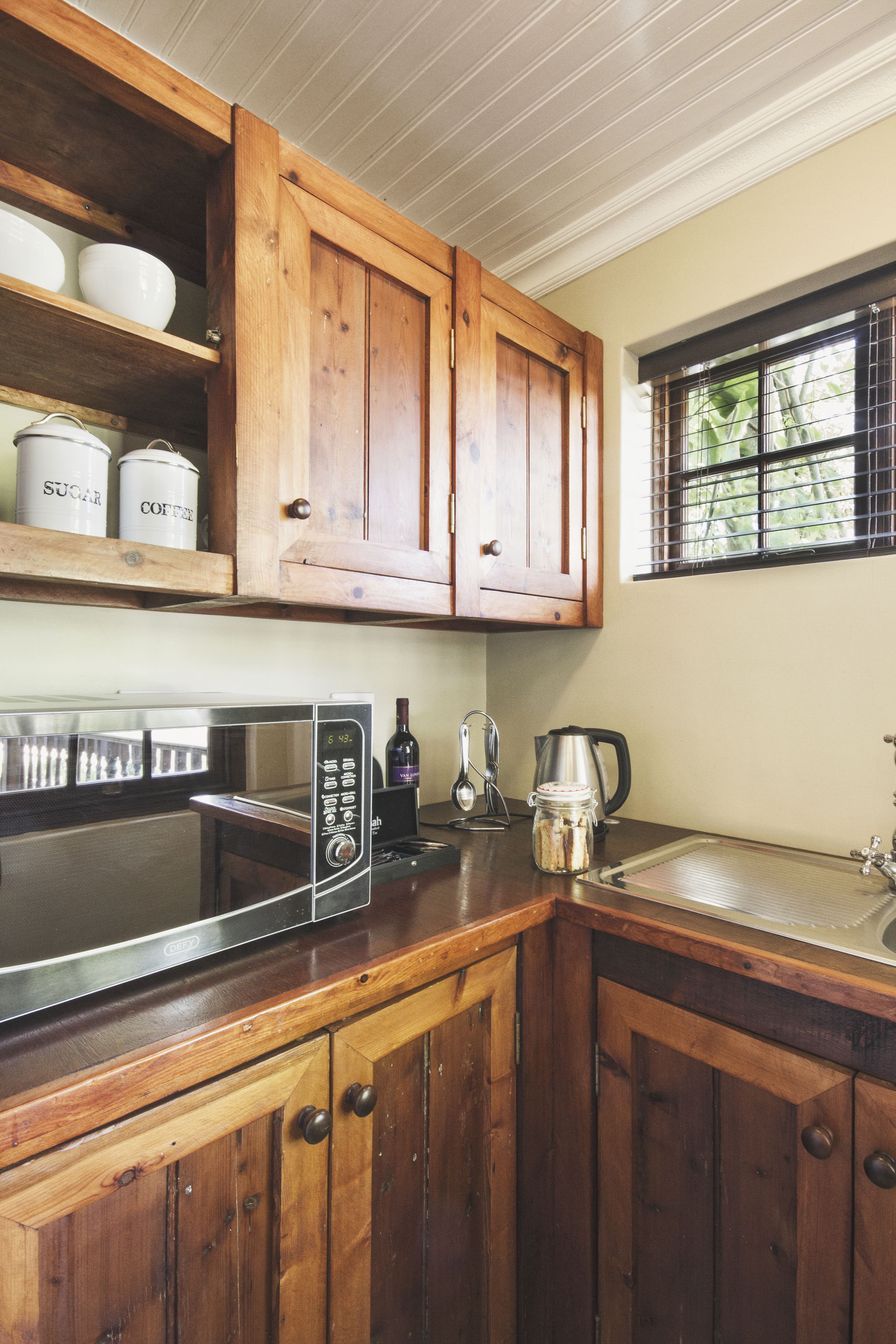 A kitchen with wooden cabinets, a microwave, a coffee maker, and a window with a view of greenery.