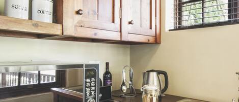 A kitchen with wooden cabinets, a microwave, a coffee maker, and a window with a view of greenery.