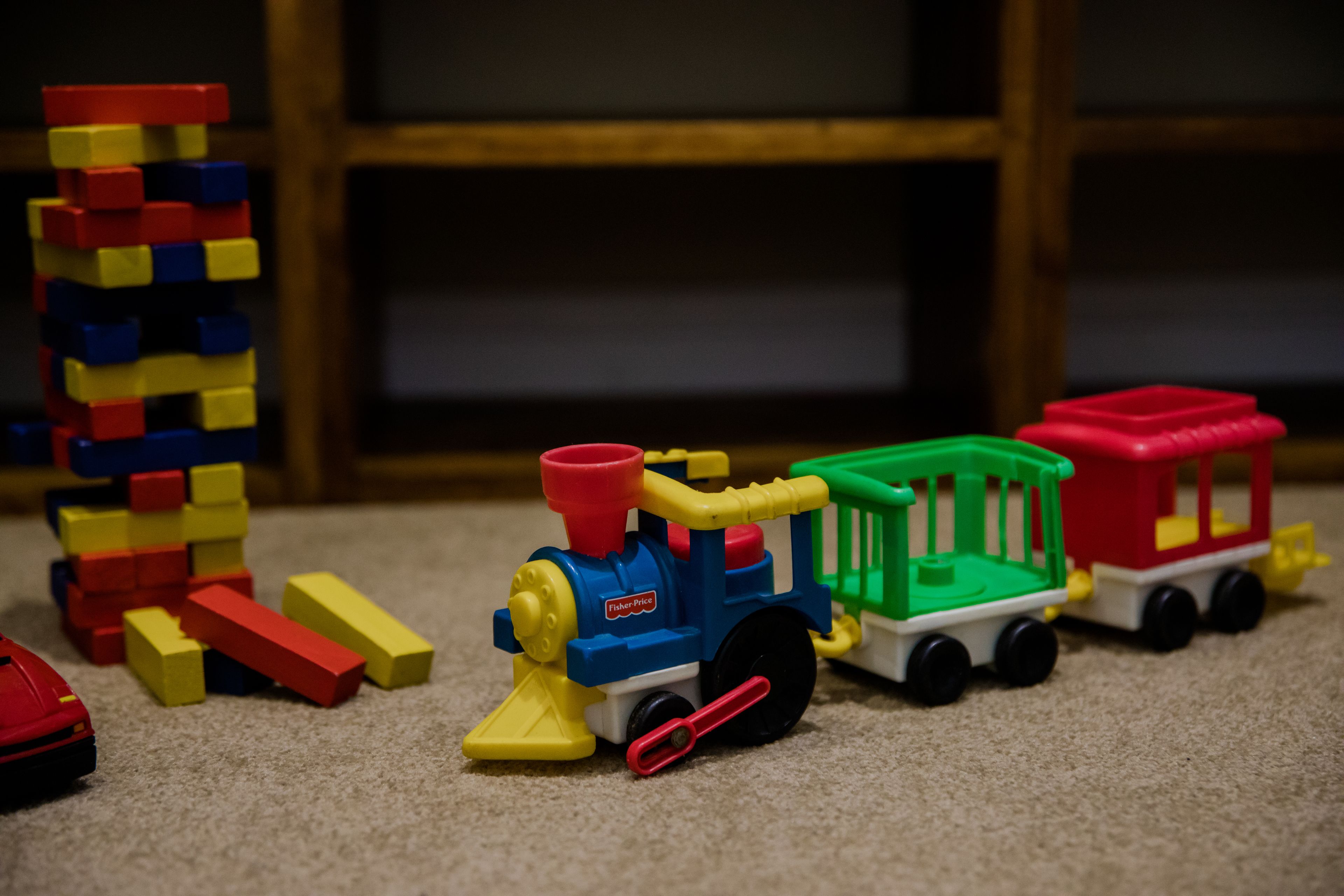 Un ensemble de jouets représentant un train, avec une locomotive rouge, des wagons verts et rouges, et des blocs de couleurs vives en arrière-plan.