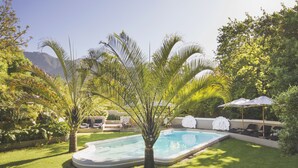 A swimming pool surrounded by lush greenery, with lounge chairs and umbrellas for relaxation. - Schoone Oordt Country House (Swellendam)