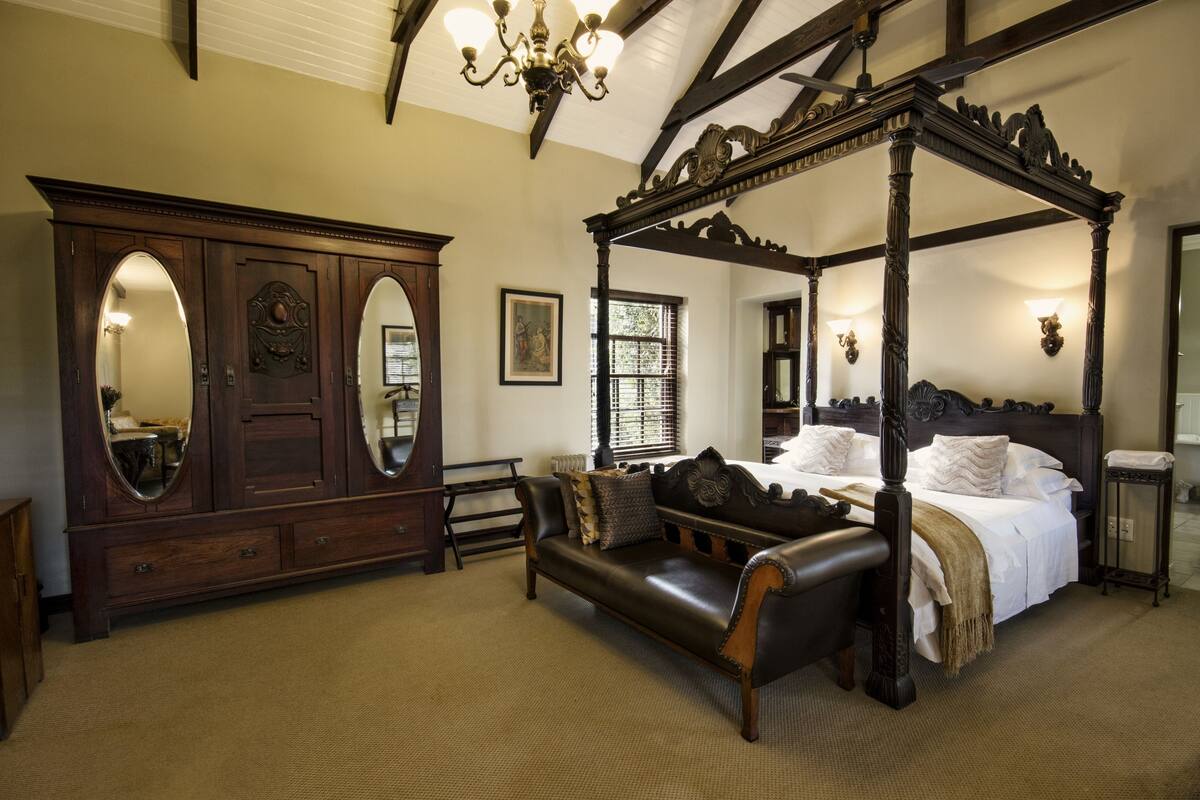 Ein traditionelles Himmelbett mit Baldachin, eine große Kommode mit Spiegelüren und ein Ledersofa in einem gut beleuchteten Raum mit hoher Decke und freiliegenden Balken.
