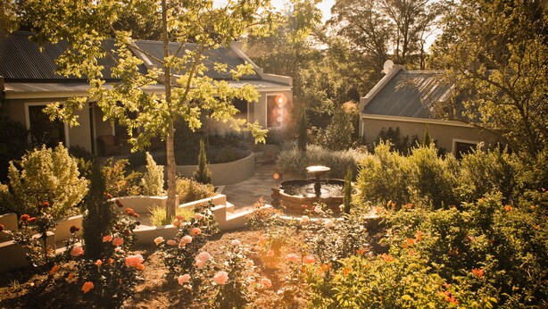 A garden with a fountain, surrounded by various plants and flowers. - Schoone Oordt Country House (Swellendam)