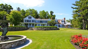 Une grande maison à deux étages, dotée d’une pelouse bien entretenue et d’une fontaine en pierre.