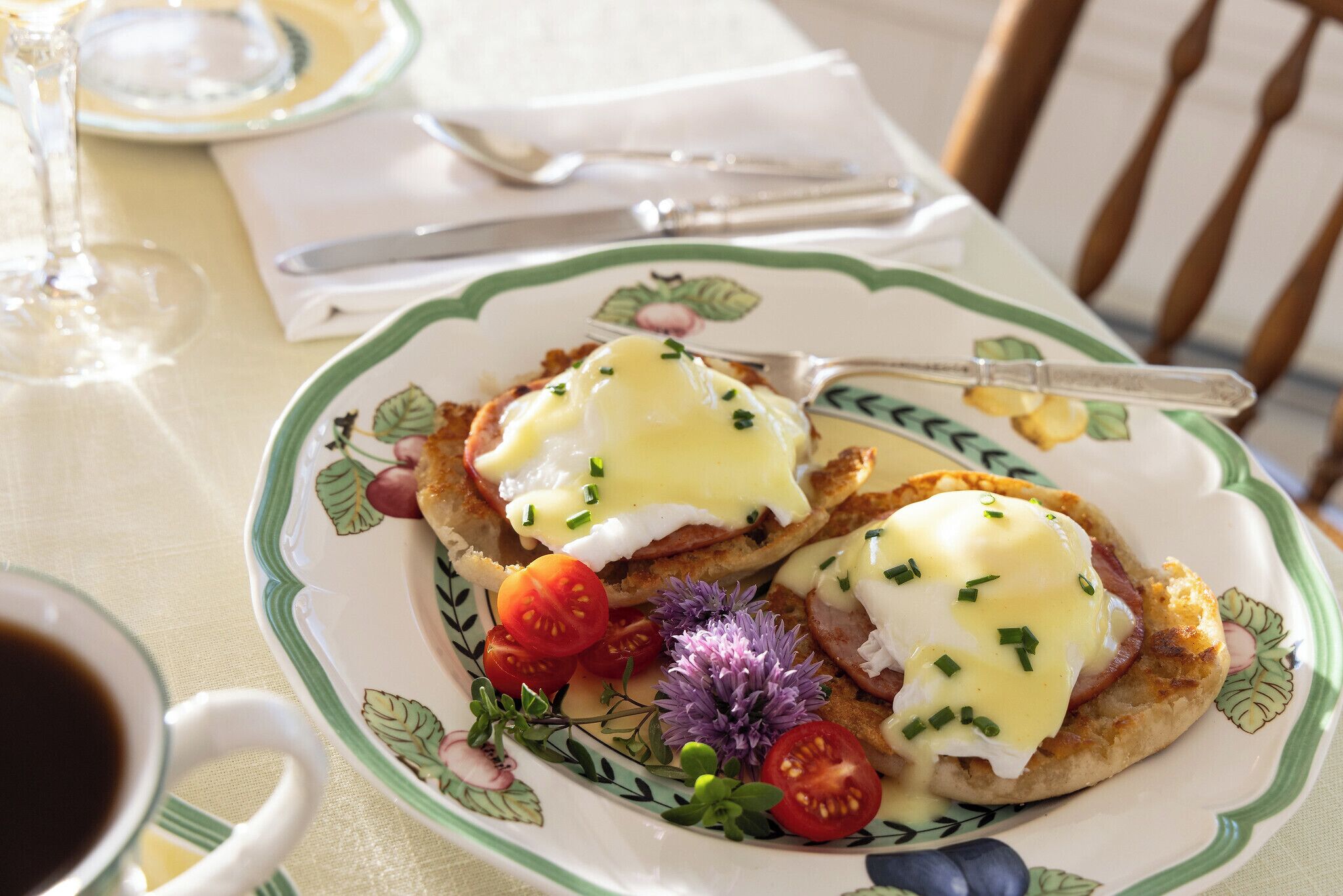 A plate with eggs Benedict, garnished with chives and cherry tomatoes, on a floral-patterned plate.