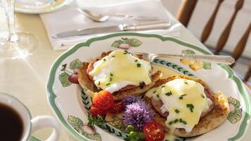 A plate with eggs Benedict, garnished with chives and cherry tomatoes, on a floral-patterned plate.