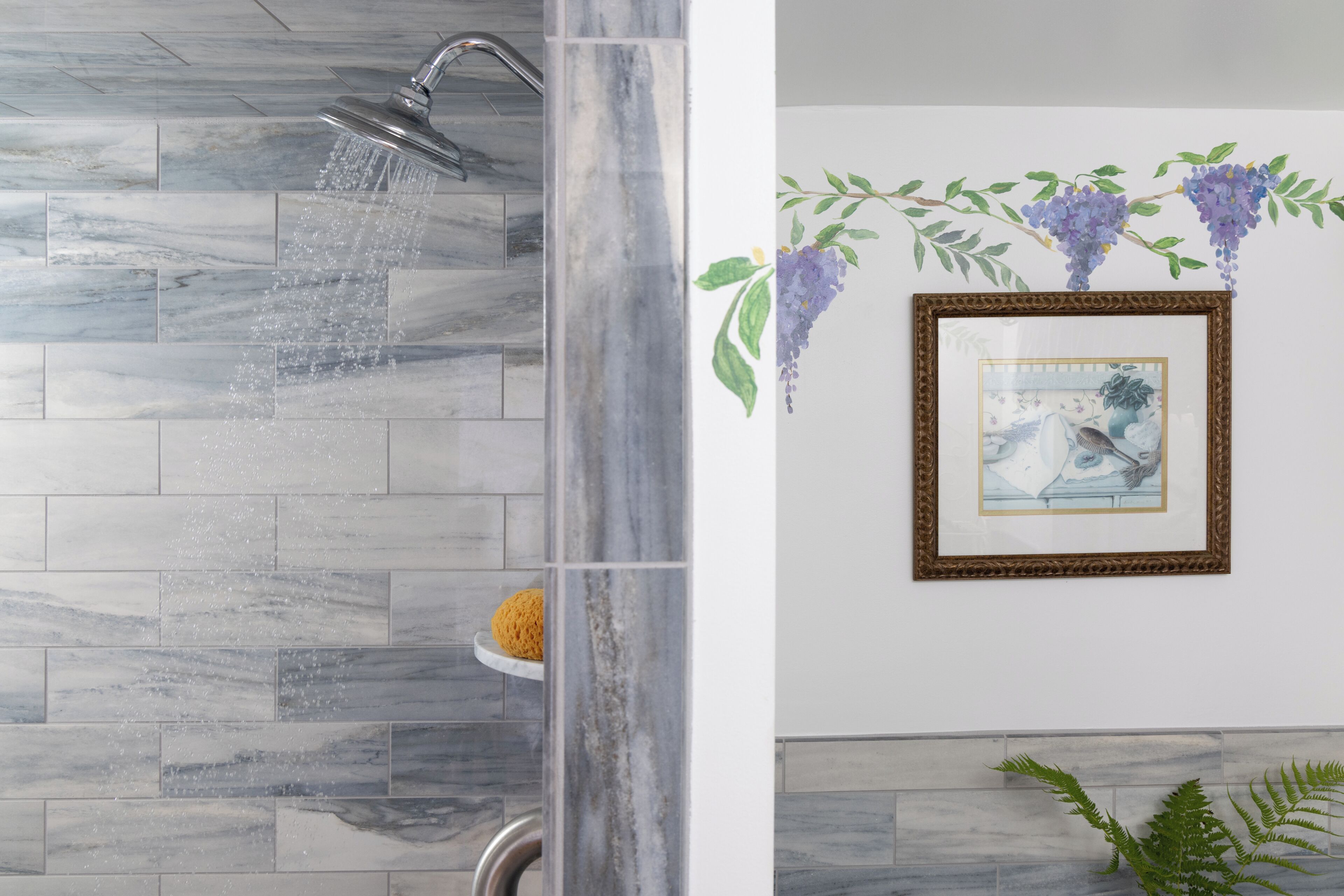 A bathroom with a shower, marble tiles, a framed picture, and a plant.
