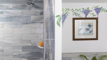 A bathroom with a shower, marble tiles, a framed picture, and a plant.