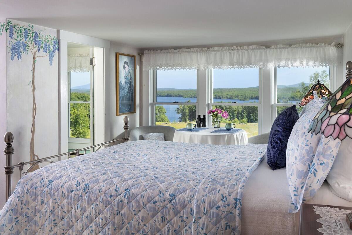 Ein Schlafzimmer mit einem großen Bett, Seeblick und einem Tisch mit Blumen.