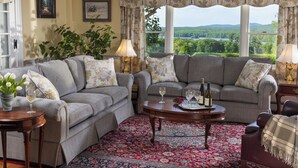 Un salon chaleureux avec deux canapés gris, un tapis rouge à motifs et une vue sur un lac et une forêt, visible à travers de grandes fenêtres.
