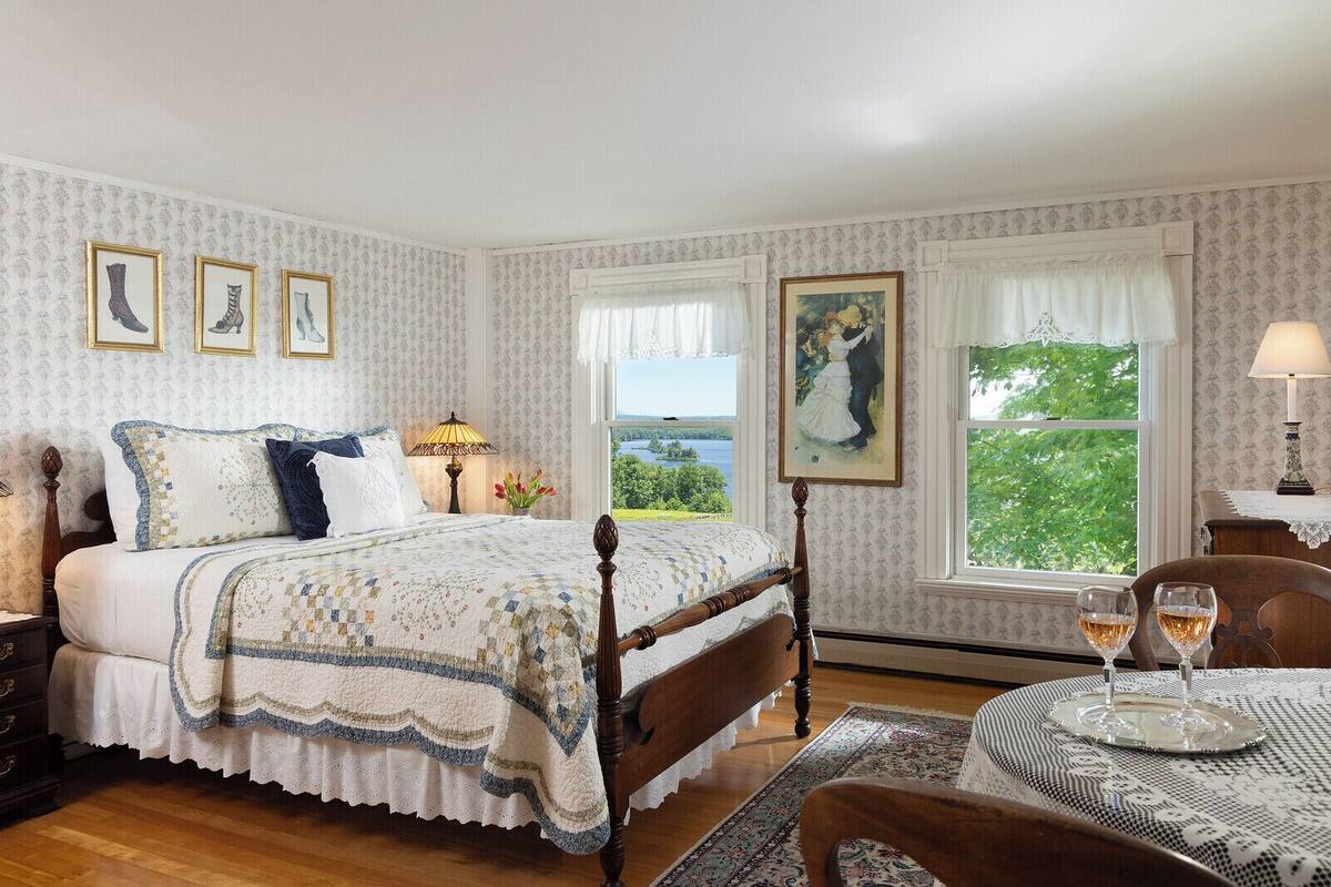Ein Schlafzimmer mit einem großen Bett, Blick ins Freie und einem Tisch mit Gläsern.