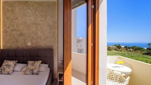 Un dormitorio con una cama grande, una mesita de noche y vistas a un balcón con mesa y sillas.
