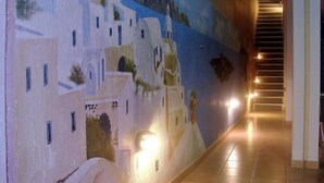 Un pasillo con un mural de edificios blancos y cielo azul.