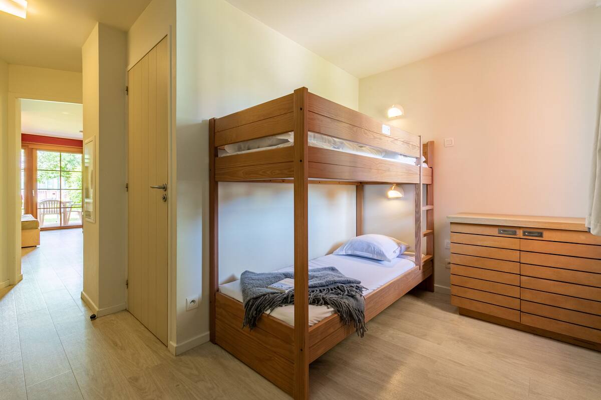A bunk bed with a wooden frame, a bedside table, and a wardrobe with multiple drawers.