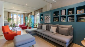 A modern living room with a grey sectional sofa, a red armchair, and a blue accent wall with framed photos and certificates. - Pierre & Vacances Résidence Le Clos d'Eguisheim (Eguisheim)