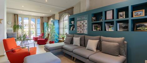 Una sala moderna con un sofá seccional gris, un sillón rojo y una pared azul decorada con fotos y diplomas enmarcados.
